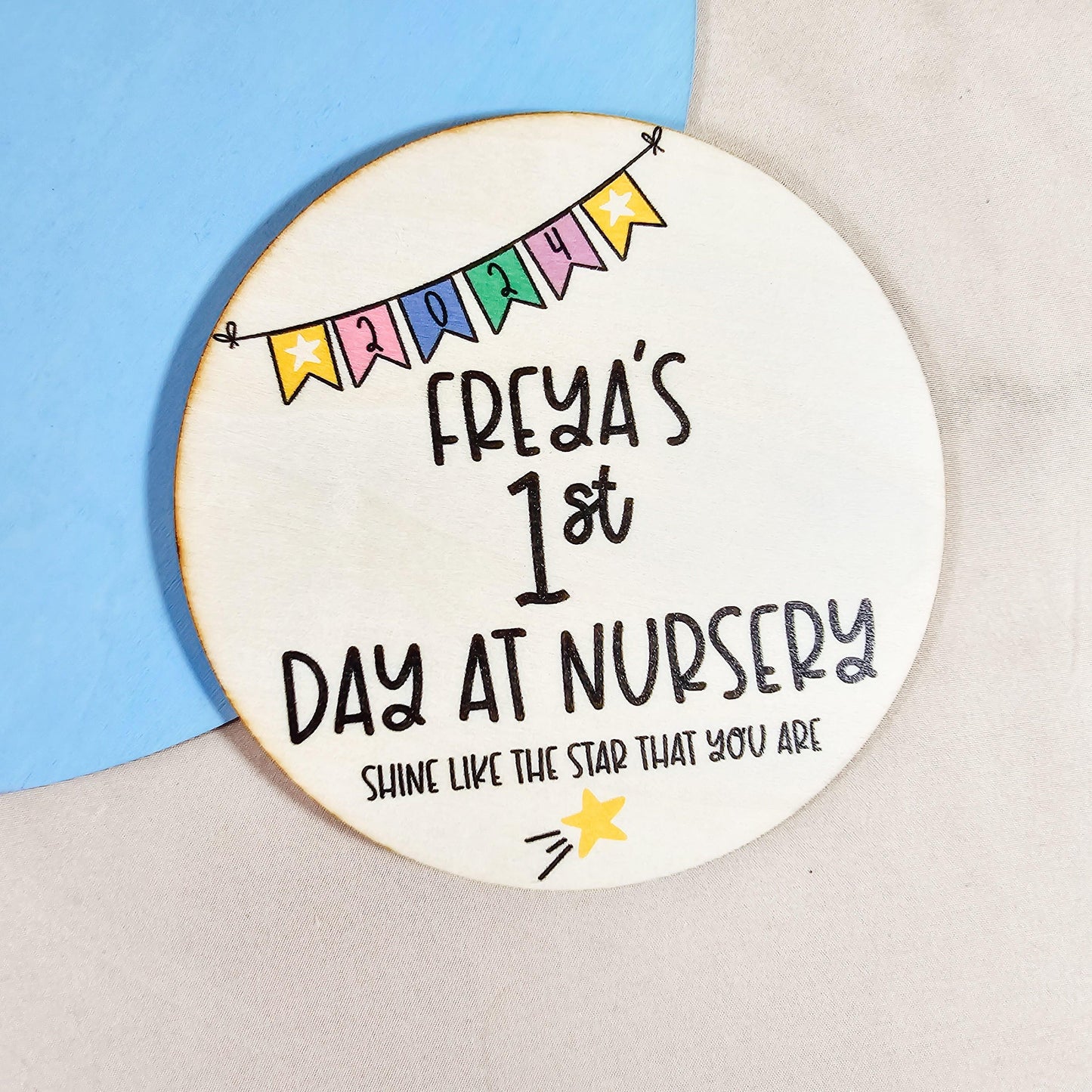 a circular wooden sign with 'names first day at nursery' on, with colourful bunting and a shooting star