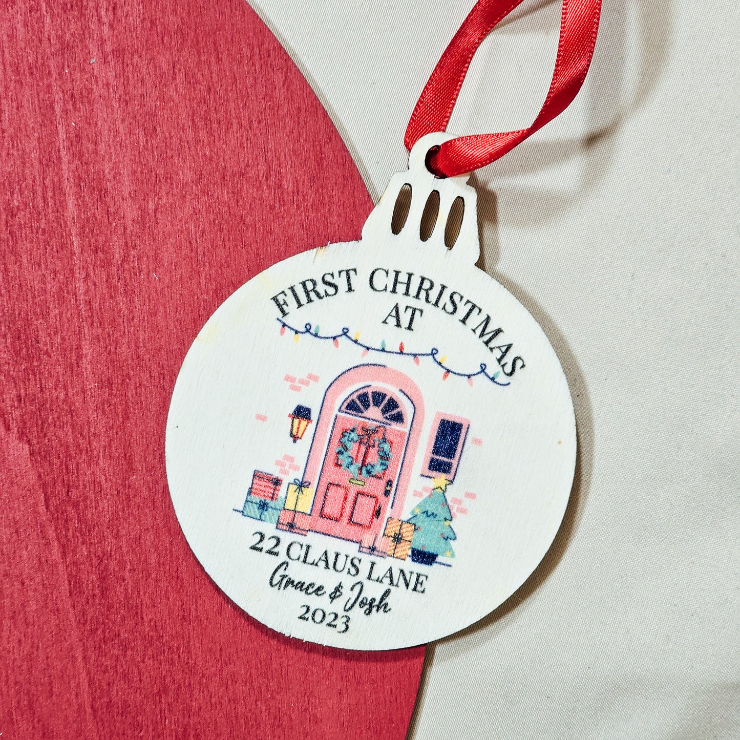 Personalised wooden bauble with "First Christmas in Our New Home" text, featuring the couple's names, address, and year printed. Comes with ribbon for hanging.