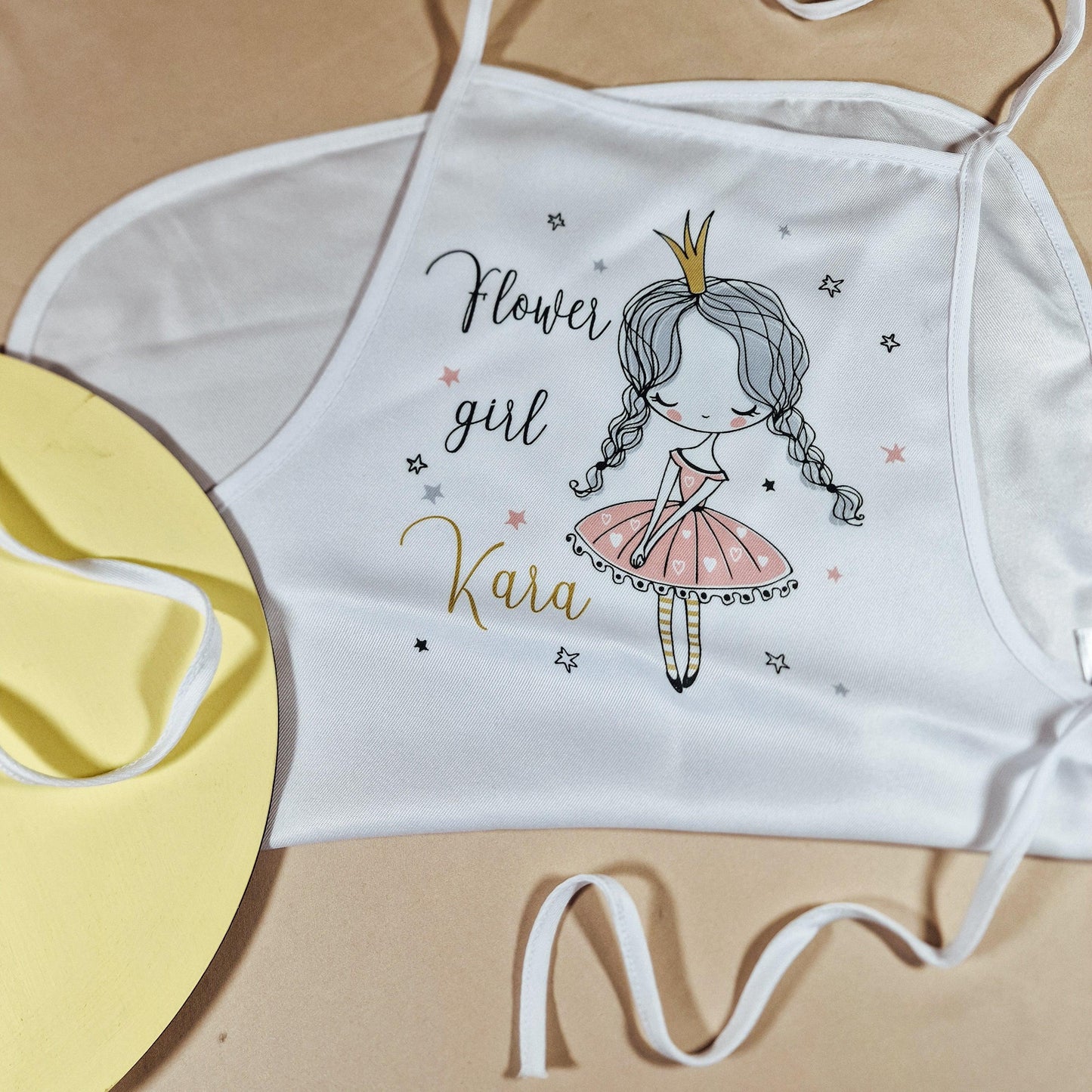 A white apron with 'flower gir' printed on and a drawing of a girl wearing a crown