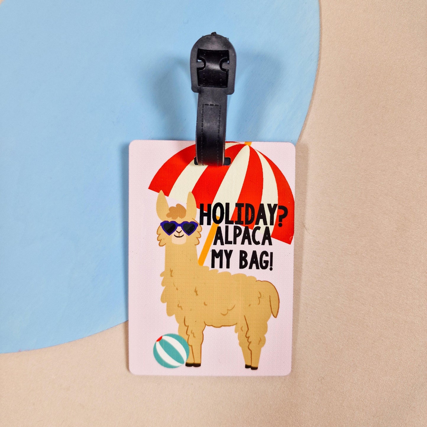 a luggage tag with an alpaca wearing sunglasses on, with a beach ball and parasol