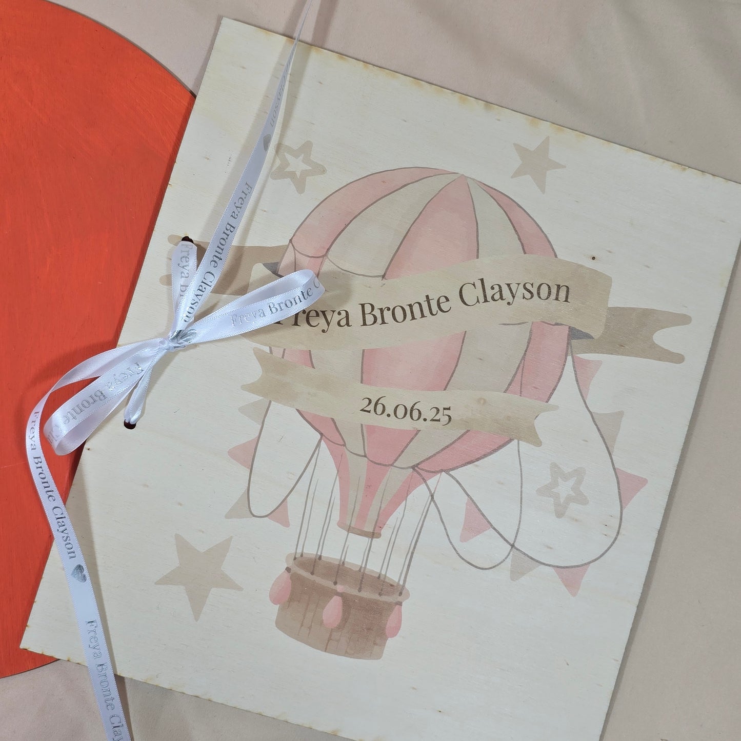 Personalized baby shower invitation with hot air balloon design and ribbon on a beige background
