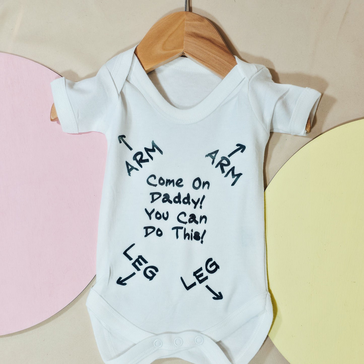 White baby vest with the text “Come on Daddy, you can do this!” and printed instructions for where baby’s arms and legs go, designed as a humorous guide for new dads.