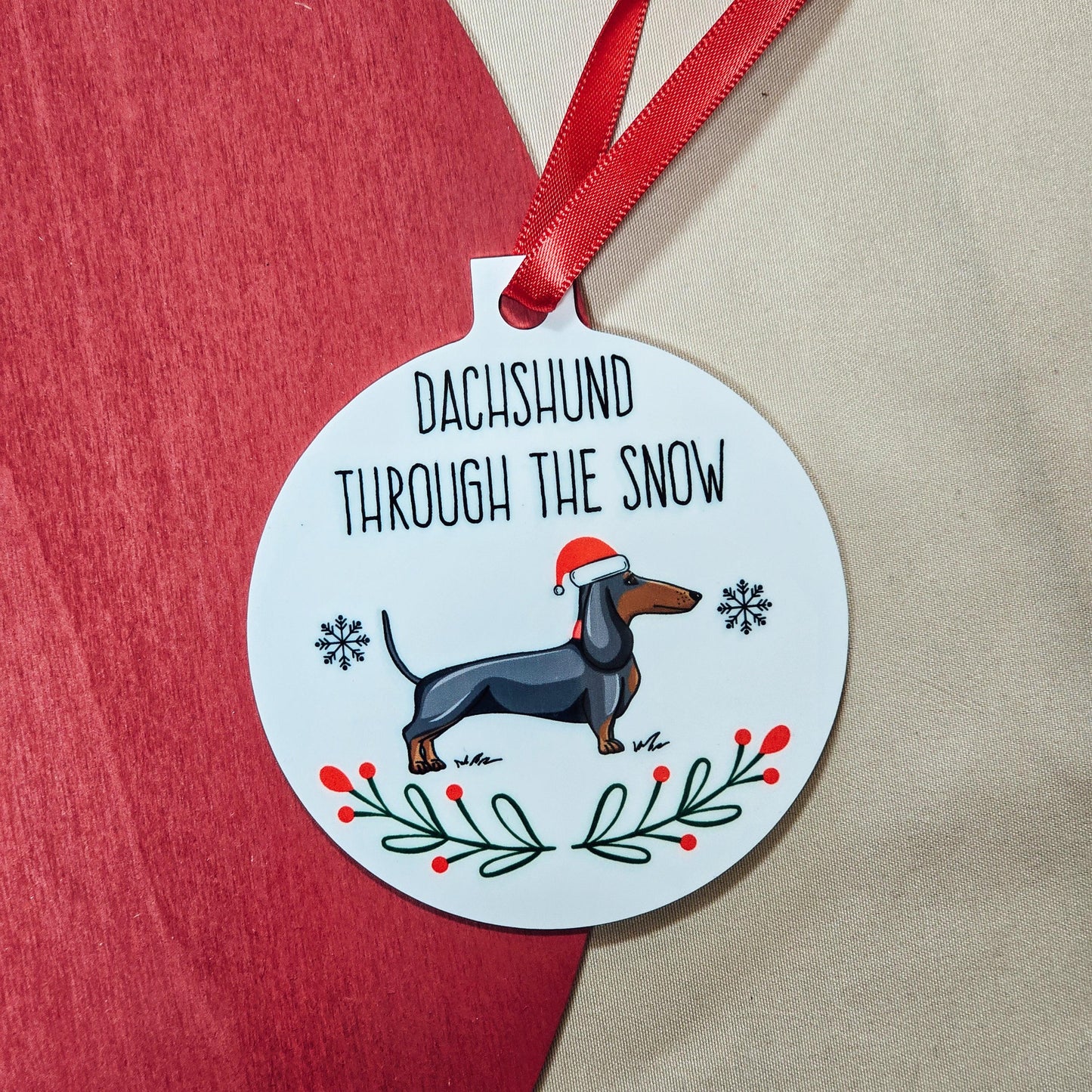 Personalised metal bauble featuring a dachshund wearing a Santa hat with 'Dachshund Through the Snow' text, includes ribbon for hanging.