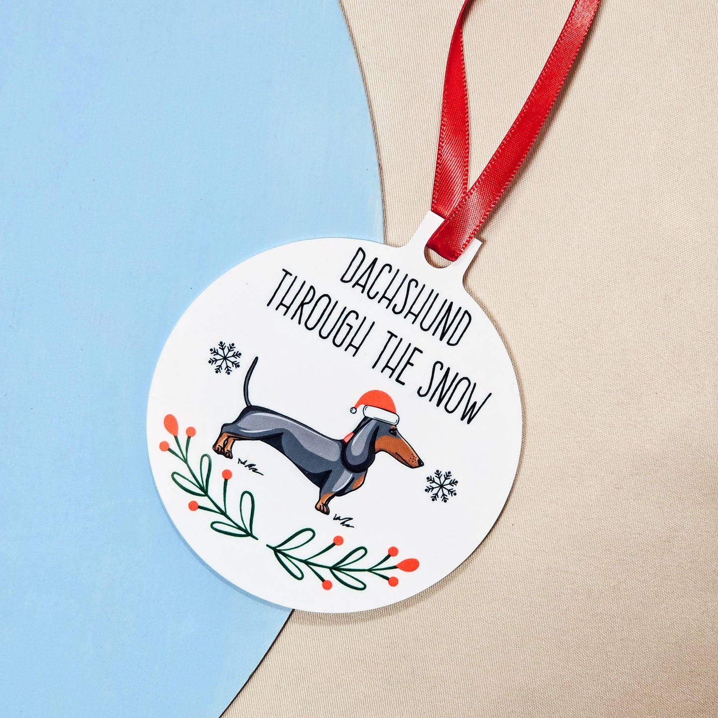 Personalised metal bauble featuring a dachshund wearing a Santa hat with 'Dachshund Through the Snow' text, includes ribbon for hanging.