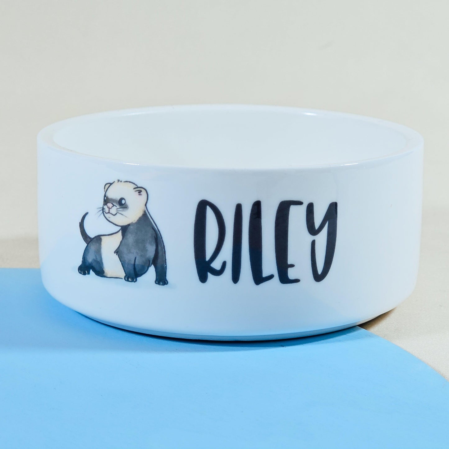 A white pet bowl featuring an adorable drawing of a ferret and personalised with the pet's name. Available in three sizes with matching pet mats.