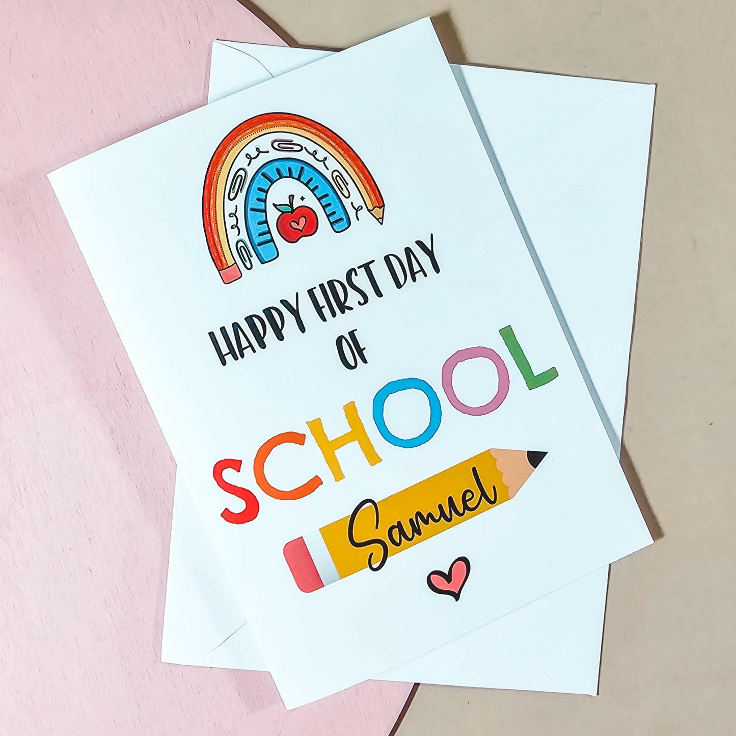White card with a rainbow printed onto it and the text 'happy first day of school' with a personalised name