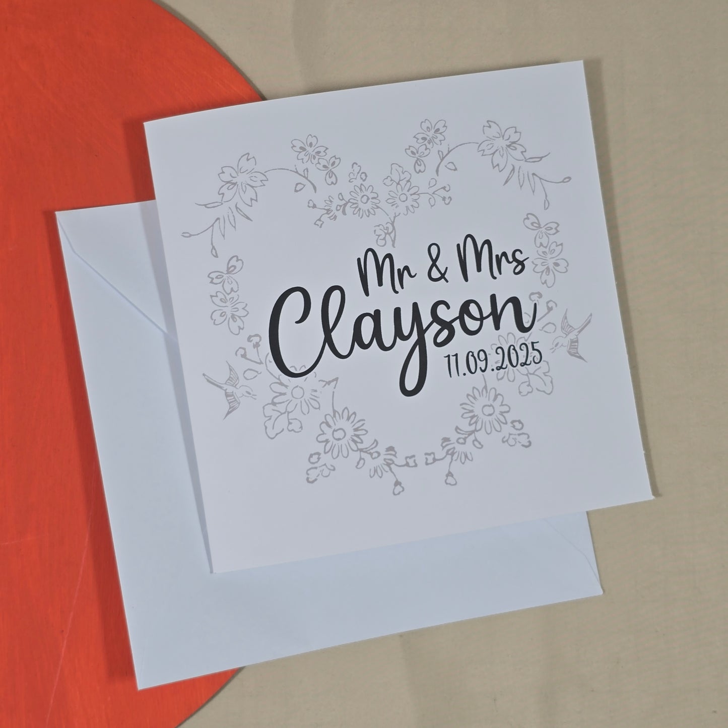 Greeting card with 'Mr & Mrs Clayson' text on a floral wreath design, with a white envelope.
