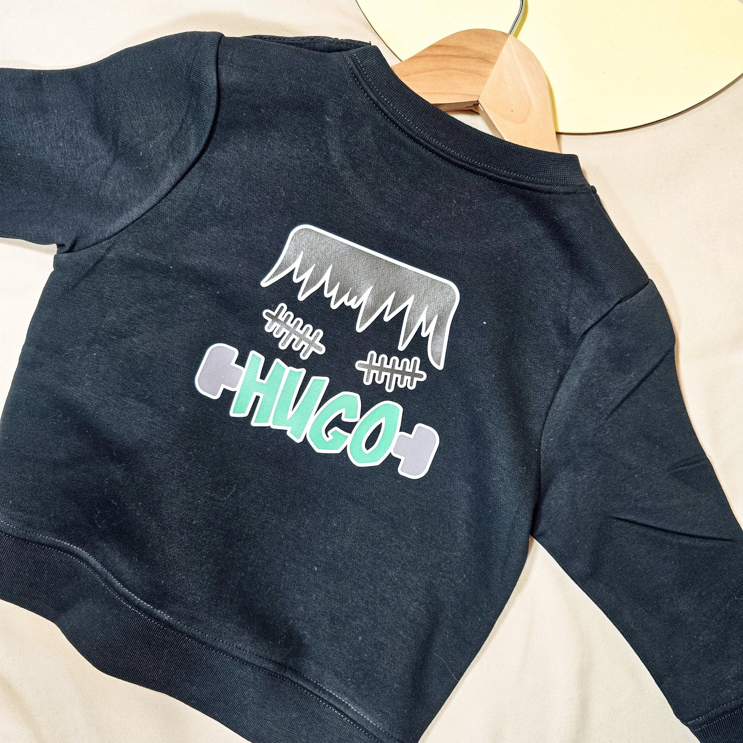 Personalised black jumper with a Frankenstein design and custom name, available in various sizes for kids, featuring an option for back printing.
