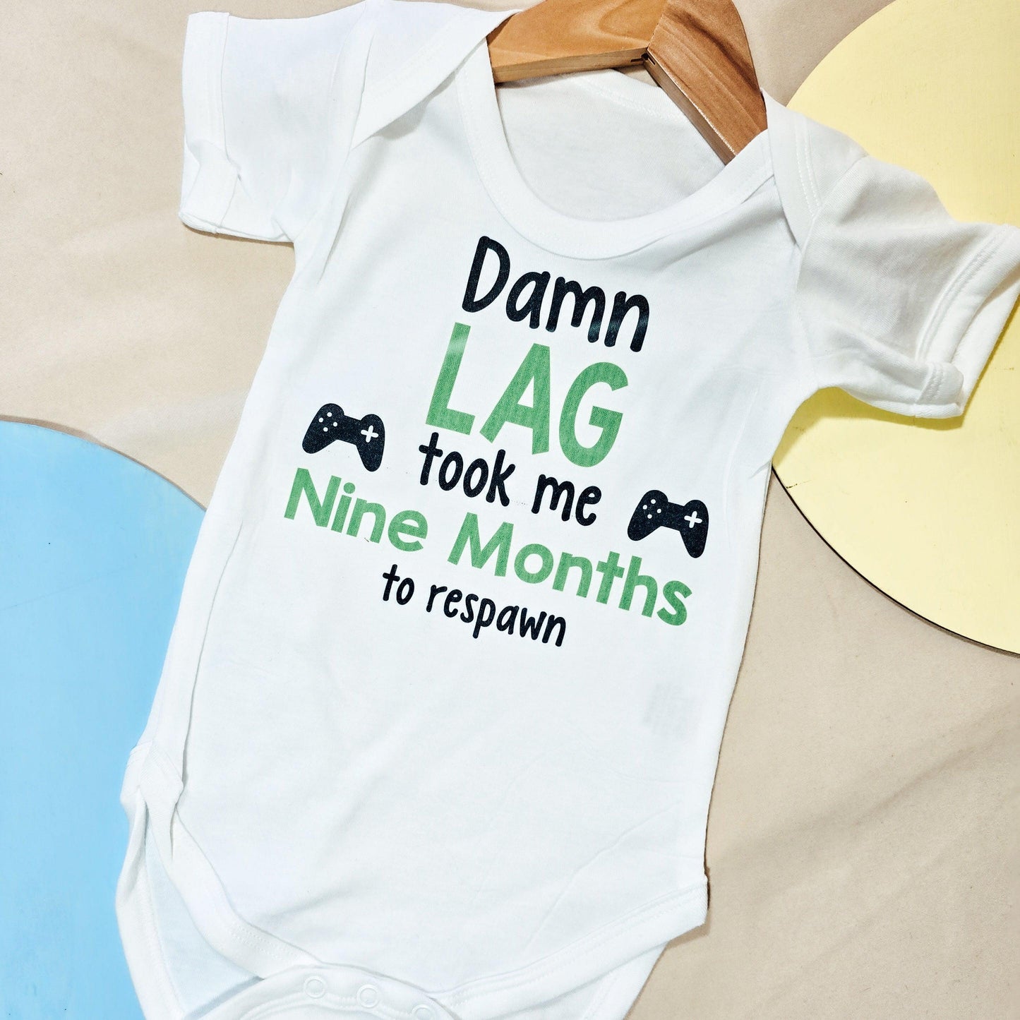 Gaming-themed baby vest with the text 'Damn lag took me 9 months to respawn,' perfect for gamer parents.