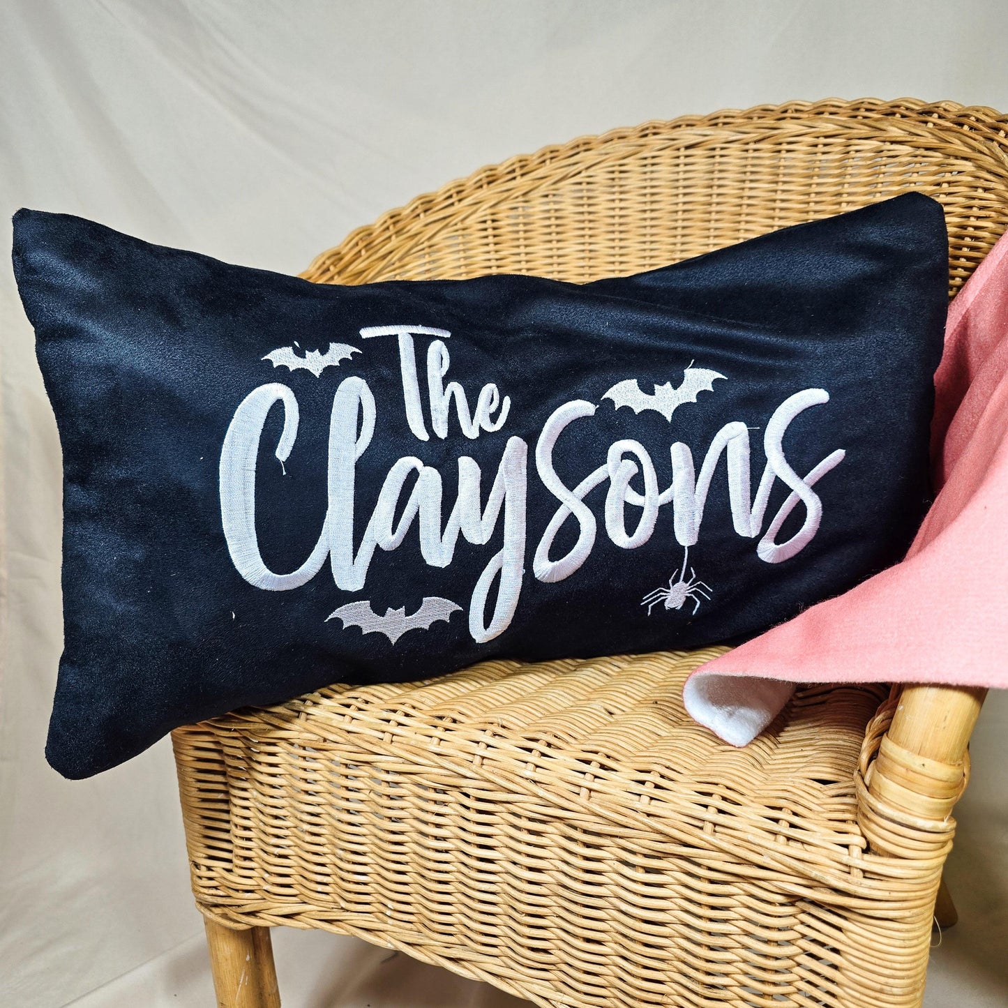 A 50x30cm faux suede cushion cover with a white embroidered family name, featuring bats and a spider design. Perfect for adding a spooky, personalised touch to Halloween home decor.