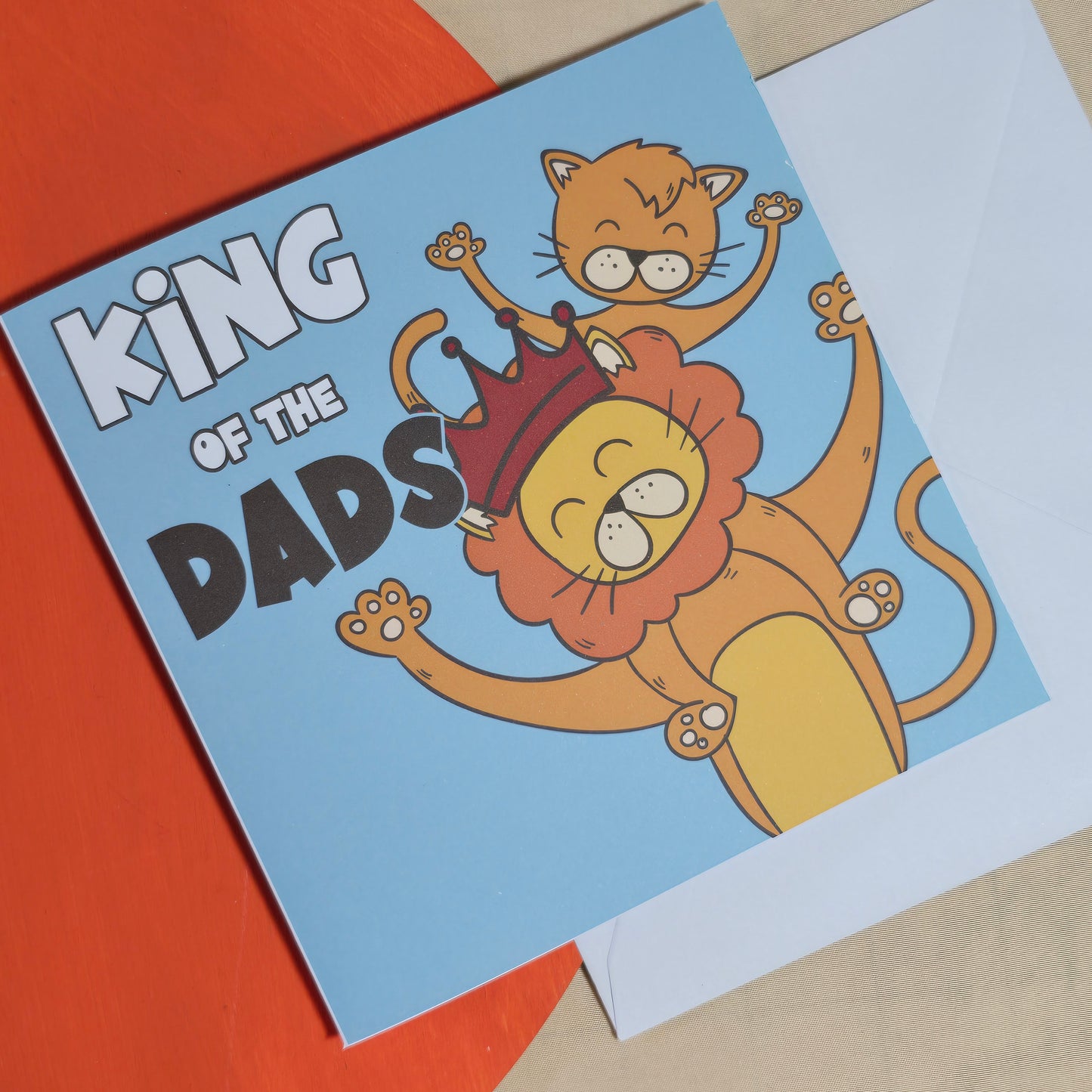 Card with cartoon lion and cat characters and 'King of the Dads' text on a blue background.