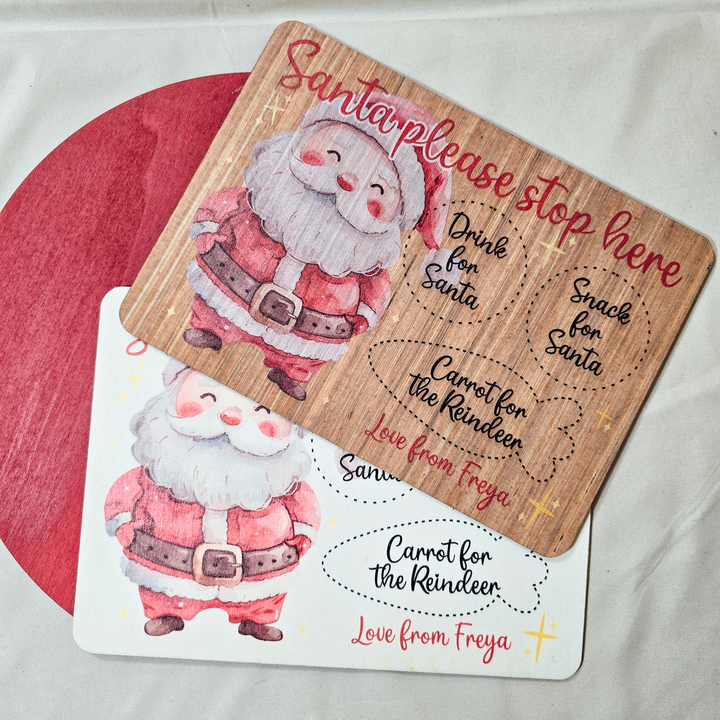 A personalised wooden Santa treat board with engraved spaces for a drink, snack, and reindeer carrot. Available in light or dark wood, with a festive Santa design and personalised name(s) at the bottom.