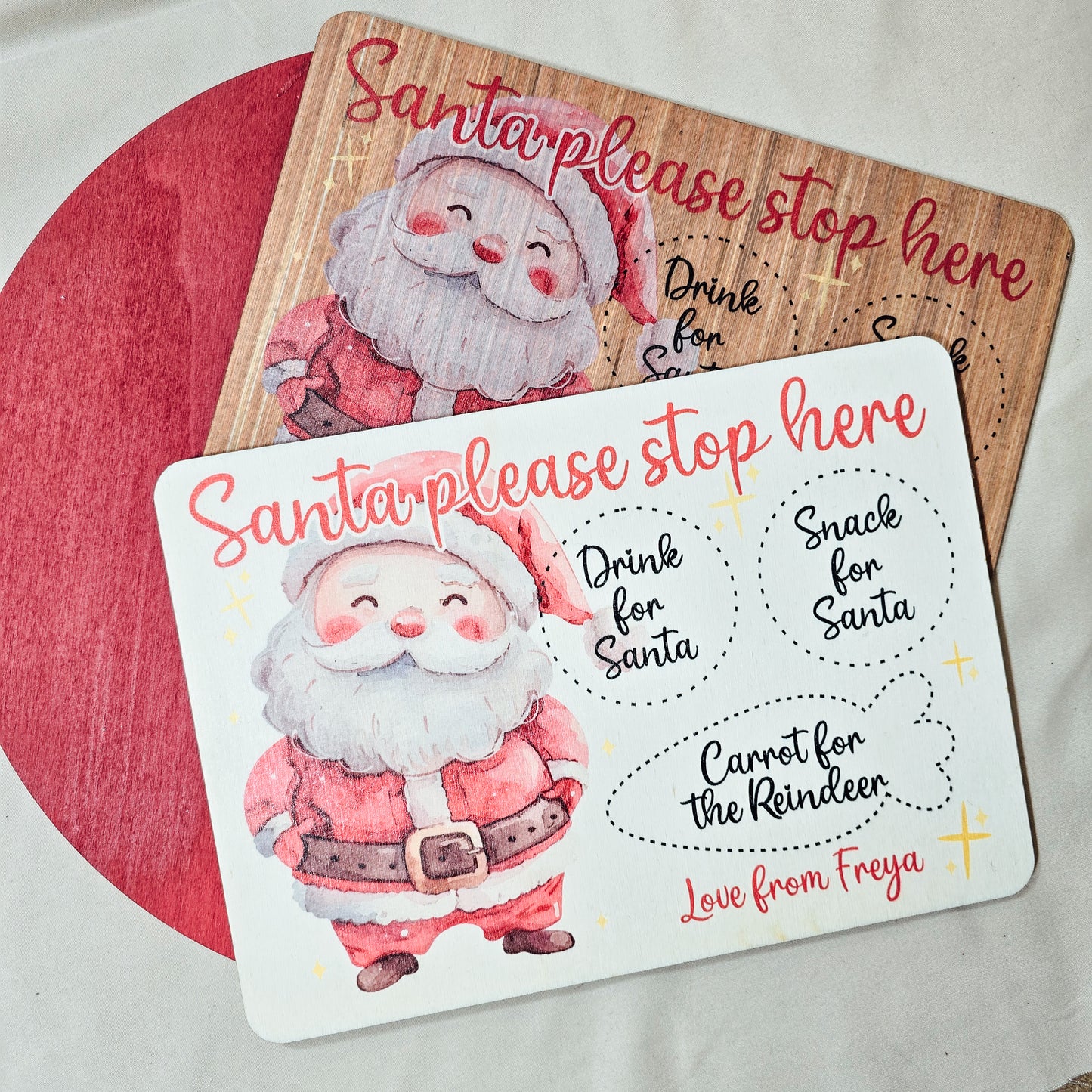 A personalised wooden Santa treat board with engraved spaces for a drink, snack, and reindeer carrot. Available in light or dark wood, with a festive Santa design and personalised name(s) at the bottom.