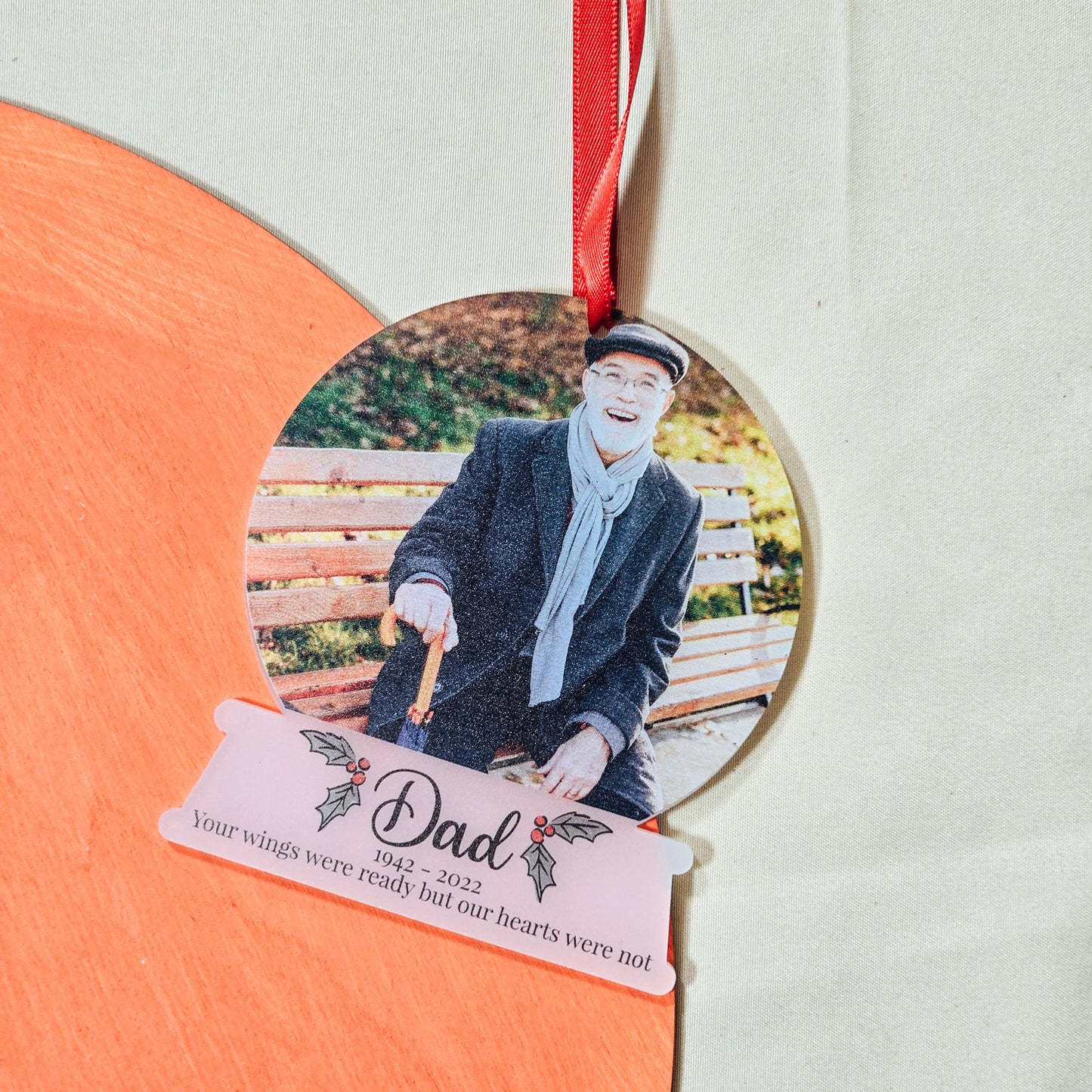 Frosted acrylic snowglobe-shaped bauble, approx. 10cm, featuring a personalised photo, name, date, and memorial message. Comes with ribbon, ready to hang on a Christmas tree in memory of a loved one.