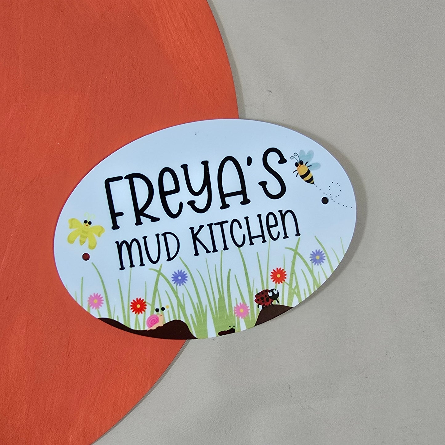 Decorative sign for 'Freya's Mud Kitchen' with cartoon elements on a red and gray background.