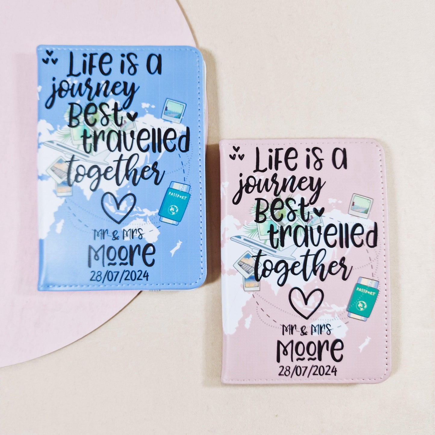 Two personalised passport covers, one blue and one pink, with the phrase 'Life is a journey best traveled together,' featuring customisable spaces for the couple's names and wedding date.