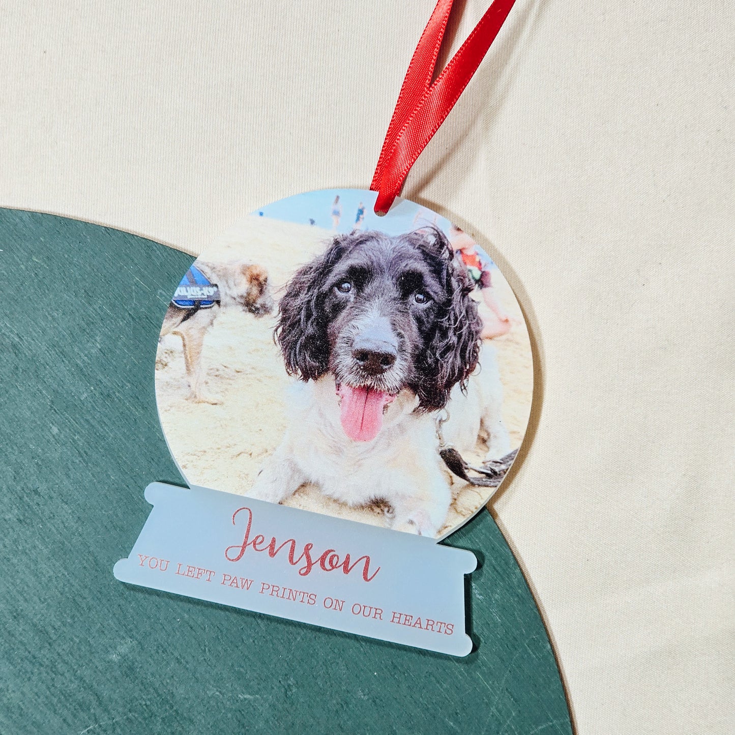 A personalised frosted acrylic snowglobe-shaped bauble featuring a photo of a pet, their name, and a memorial message. The bauble hangs from a ribbon, a touching tribute to a beloved pet on the Christmas tree.