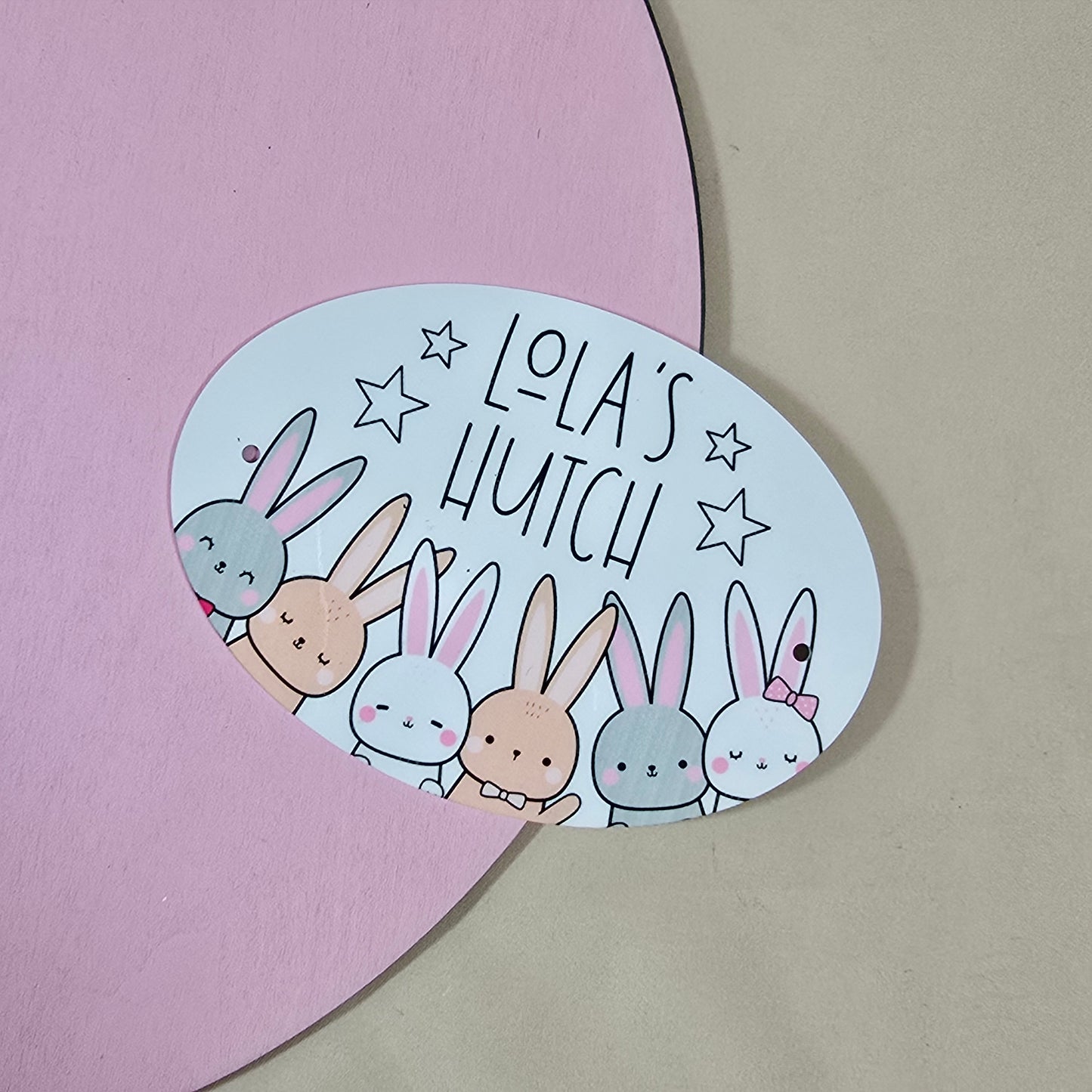 Circular sticker with cartoon bunnies and 'Lola's Hutch' text on a pink and beige background