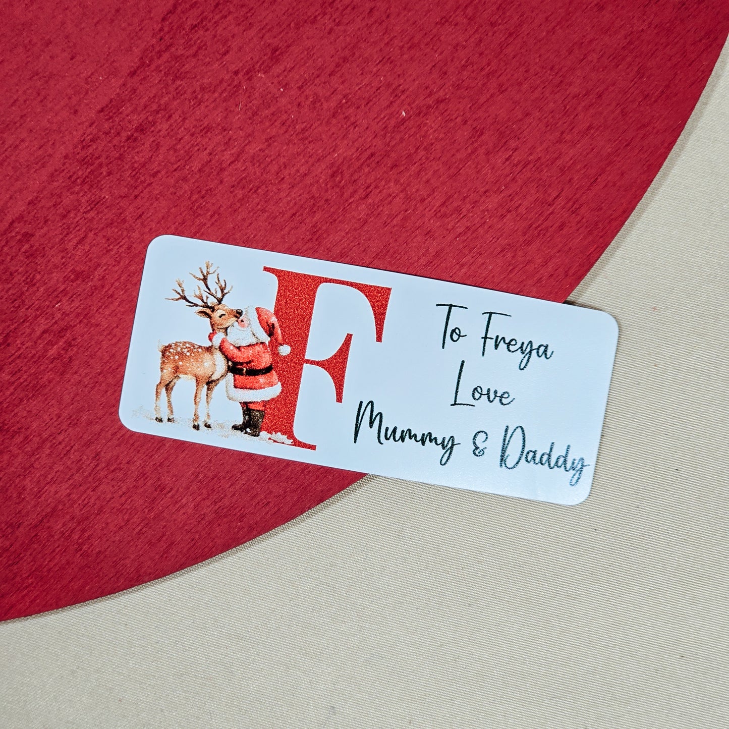 A pack of 25 customisable Christmas gift stickers, each featuring a Santa design and a personalised initial and message. The stickers are approximately 5cm in size, perfect for adding a personal touch to festive gift-wrapping.