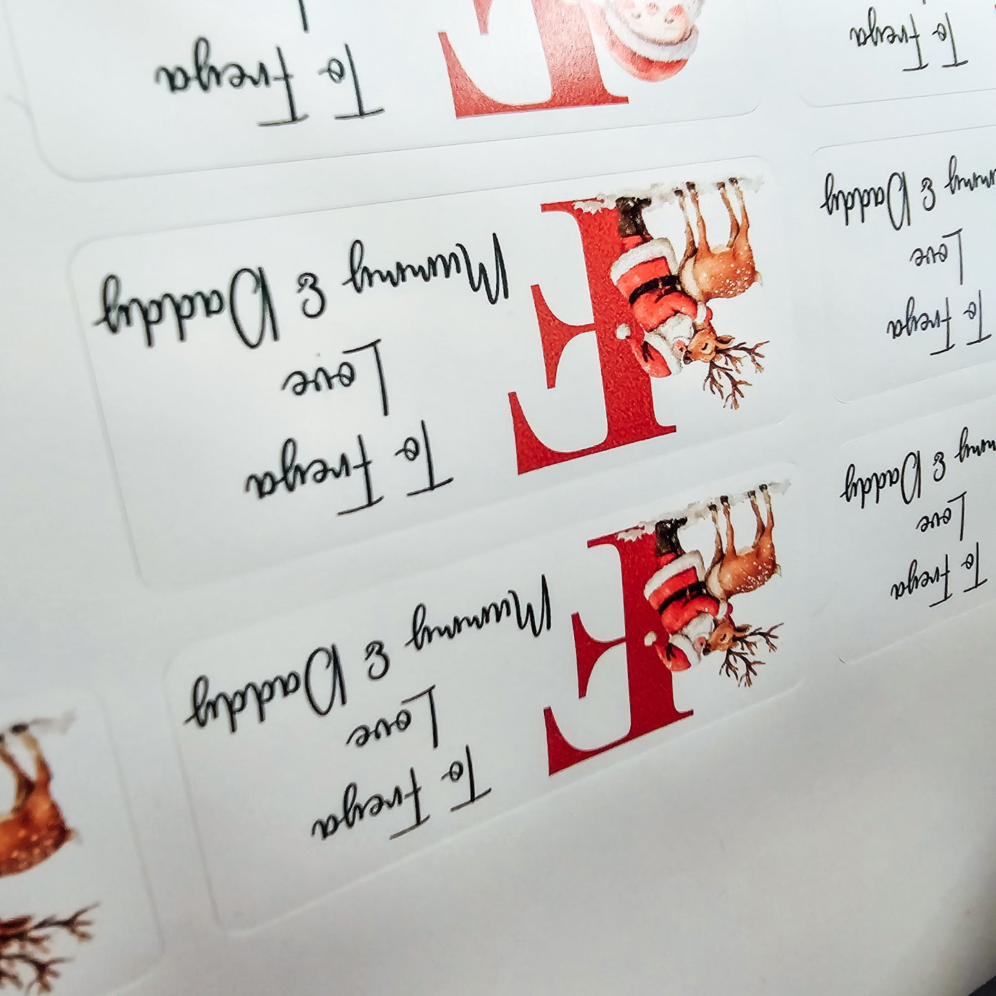A pack of 25 customisable Christmas gift stickers, each featuring a Santa design and a personalised initial and message. The stickers are approximately 5cm in size, perfect for adding a personal touch to festive gift-wrapping.
