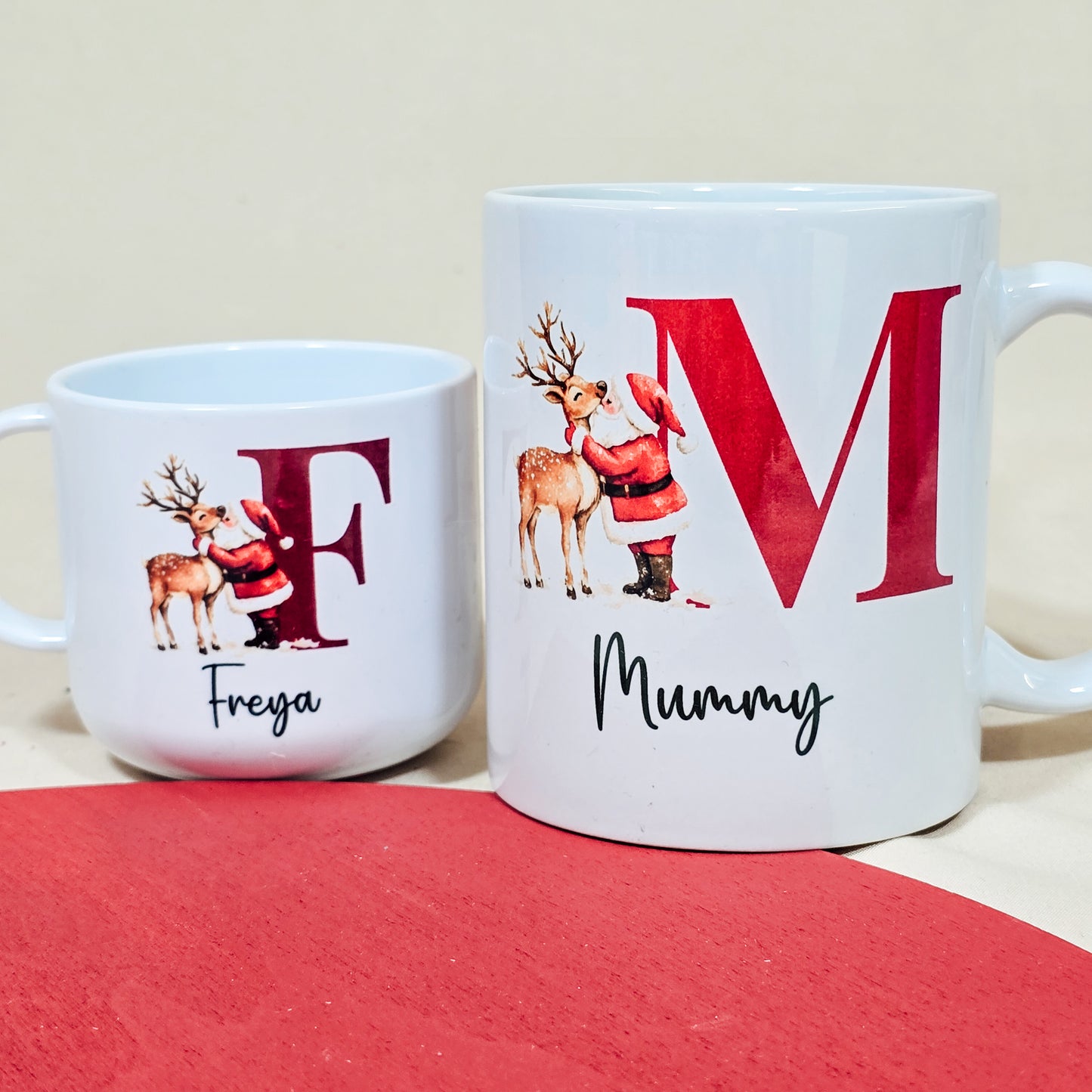 A 6oz mini children's mug featuring a festive design of Santa kissing a reindeer, personalised with a child's name and initial. The unbreakable polymer cup is perfect for little hands and makes an ideal Christmas gift, with matching adult mugs available.