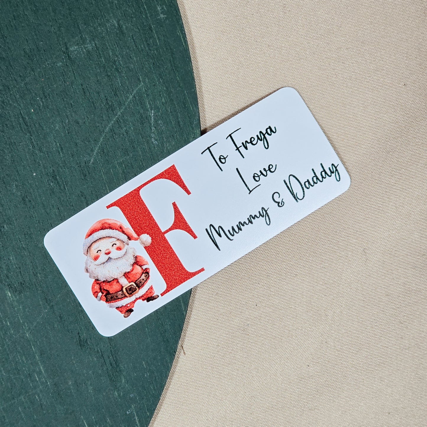 A pack of 25 customisable Christmas gift stickers, each featuring a Santa design and a personalised initial and message. The stickers are approximately 5cm in size, perfect for adding a personal touch to festive gift-wrapping.