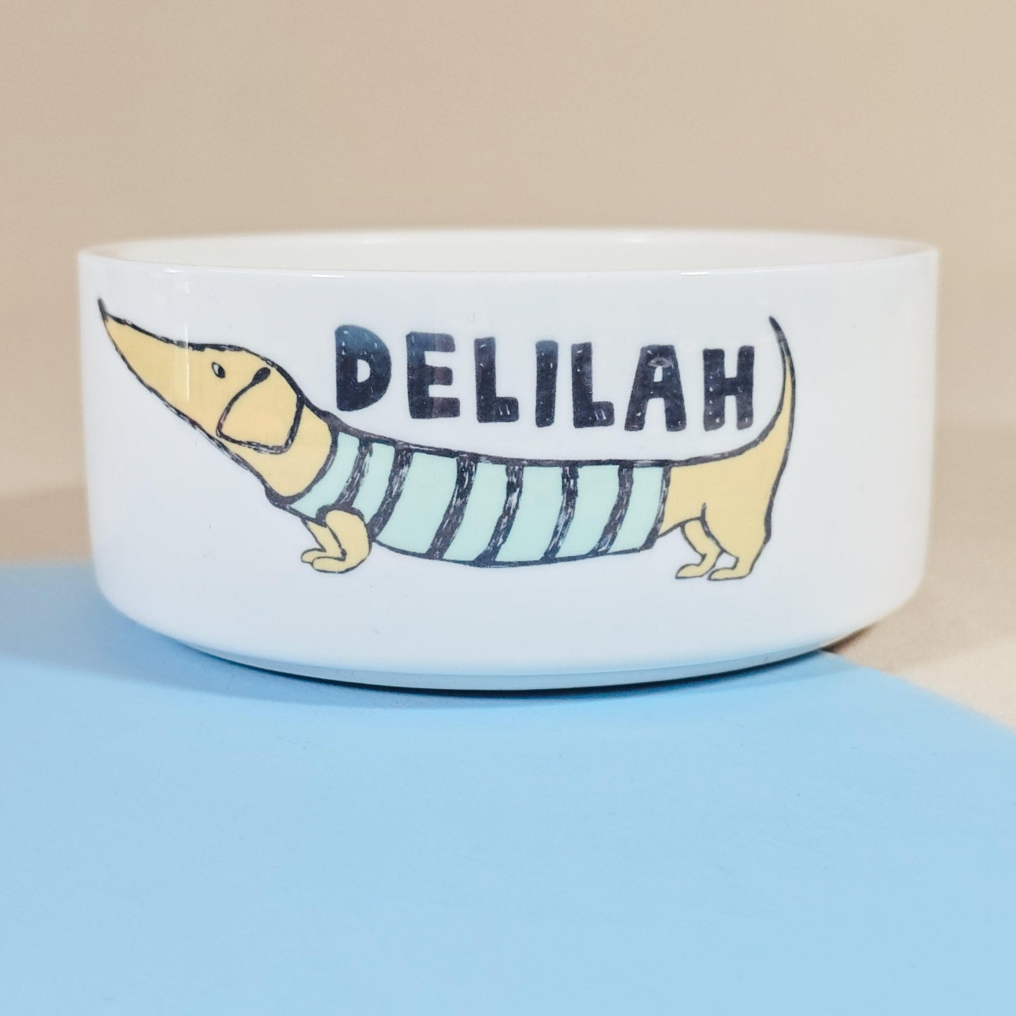 Personalised dachshund dog bowl featuring a sausage dog in a stripey jumper, with the dog's name on the bowl. Available in three sizes, perfect for any dachshund lover.