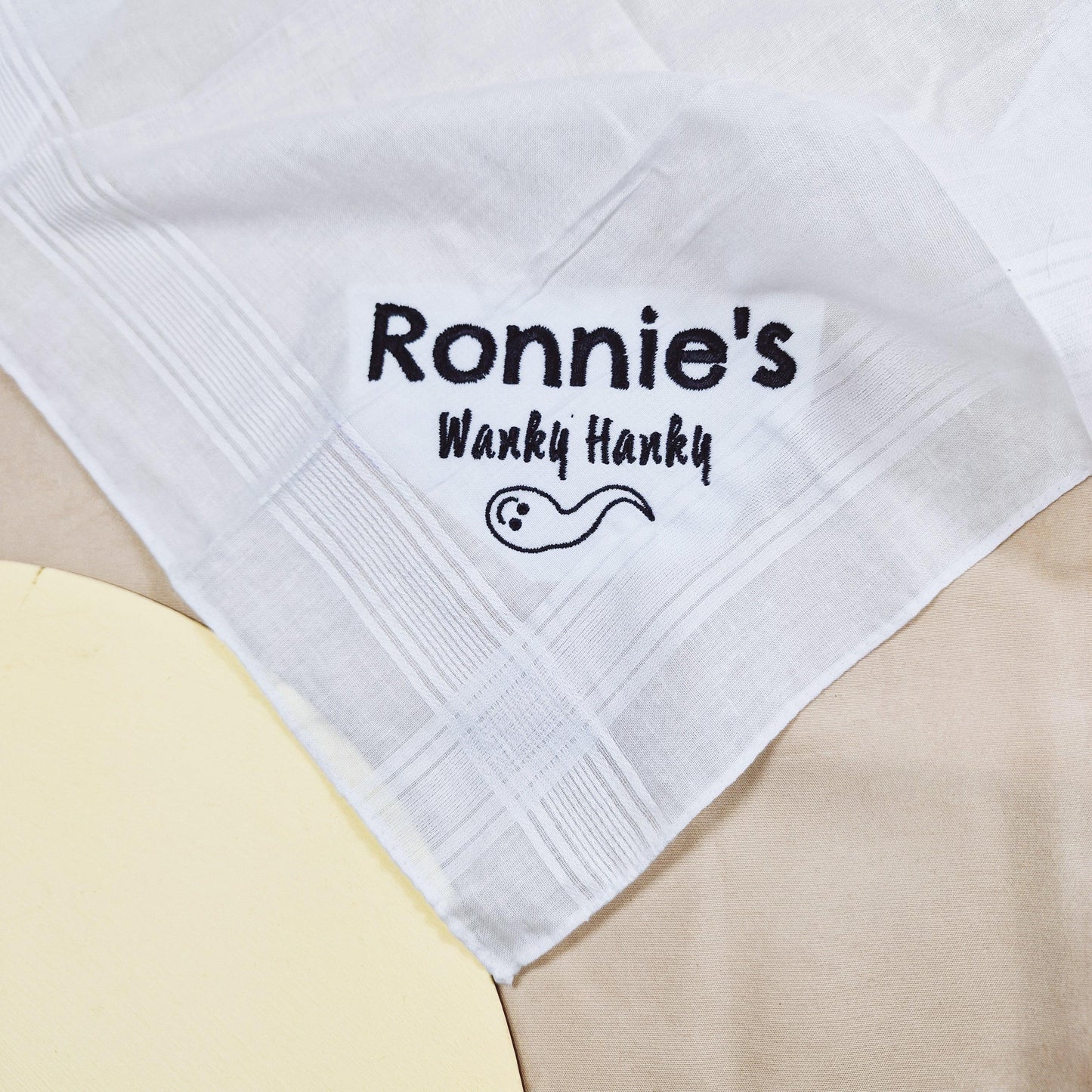 An embroidered handkerchief with the text "Names Wanky Hanky" on it. Customisable with names, this funny and unique handkerchief is perfect for a playful sex gift or humorous occasion.