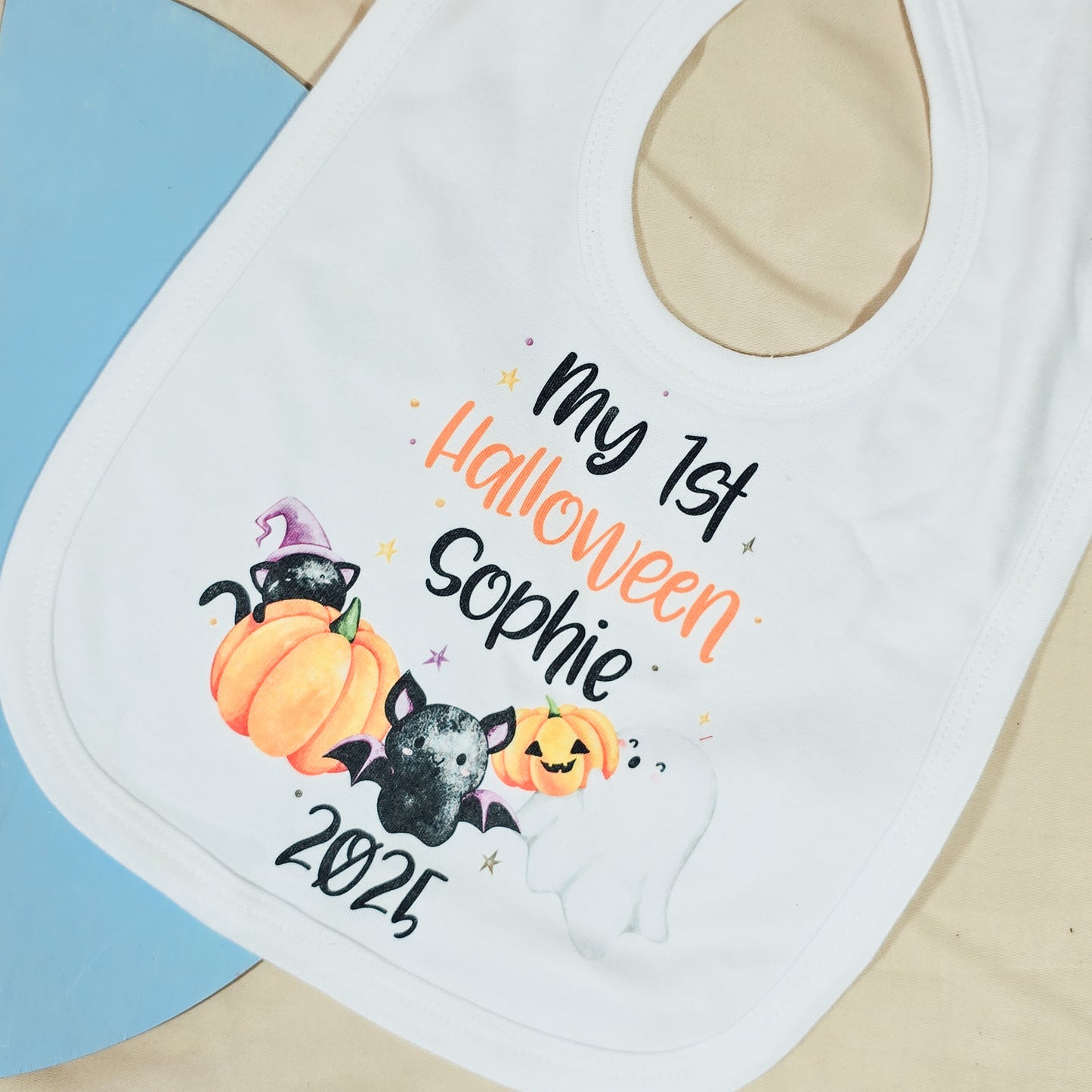 Baby bib with Halloween-themed design and text on a blue and beige background