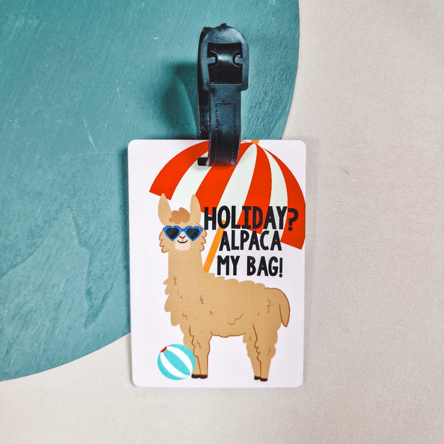 a luggage tag with an alpaca wearing sunglasses on, with a beach ball and parasol