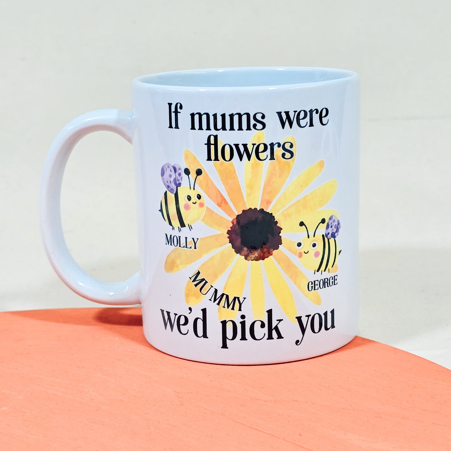 White ceramic mug with floral design, bees featuring children's names, and the text "If Mums were flowers, we'd pick you."

