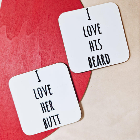 A pair of square coasters with curved edges, one saying "I Love His Beard" and the other "I Love Her Butt". Made from hardboard with a glossy, wipe-clean surface, each coaster measures approximately 9cm. Ideal for couple gifts or humorous home decor.