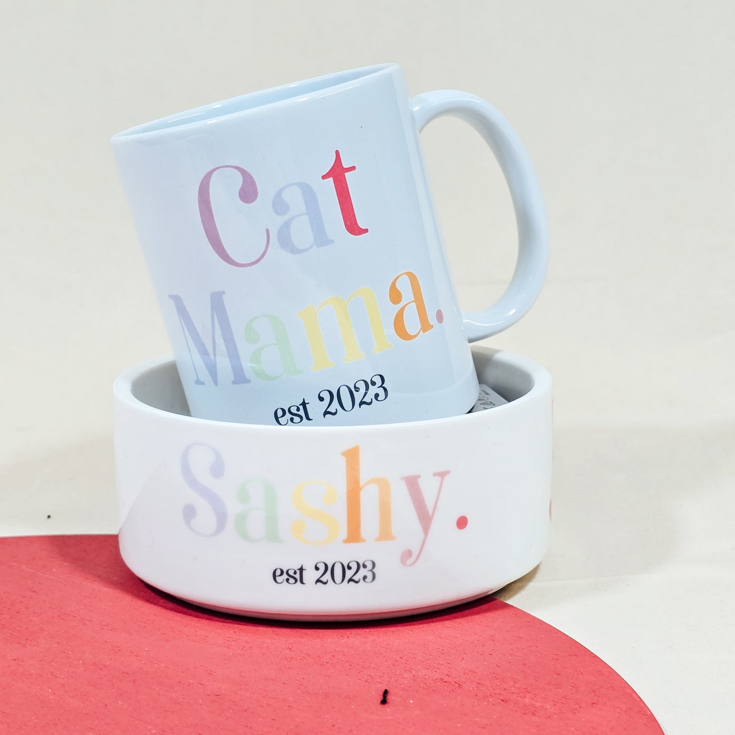 A white ceramic mug with "Cat Mama Est [Date]" in elegant script, available with a matching pet bowl in various sizes.

