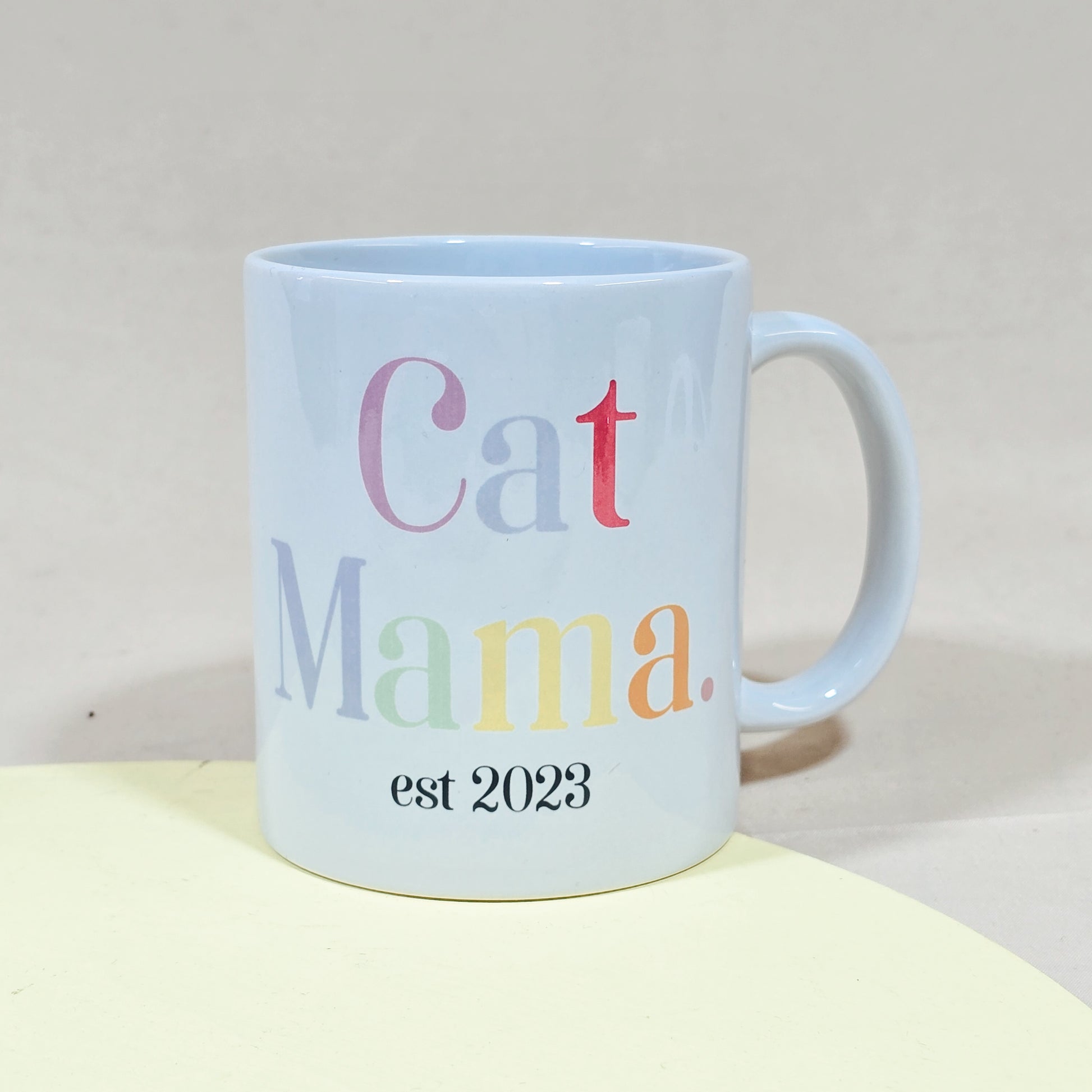 A white ceramic mug with "Cat Mama Est [Date]" in elegant script, available with a matching pet bowl in various sizes.

