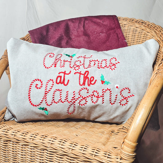 Decorative pillow with 'Christmas at the ' text on a wicker chair.
