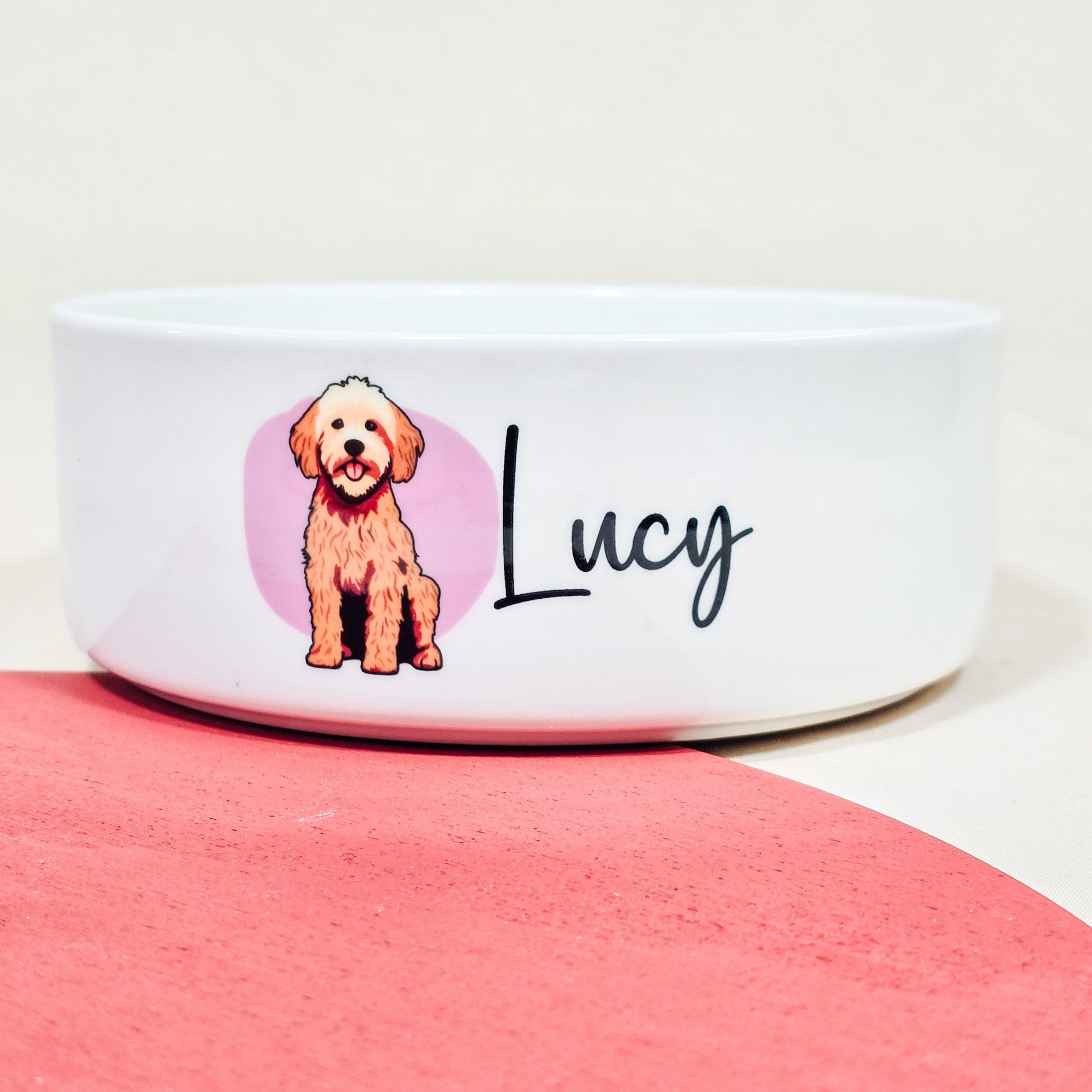 A personalised ceramic dog bowl featuring a cartoon Cockerpoo on a pink background, customisable with the dog's name. Available in small (12cm), medium (15cm), and large (18cm) sizes.