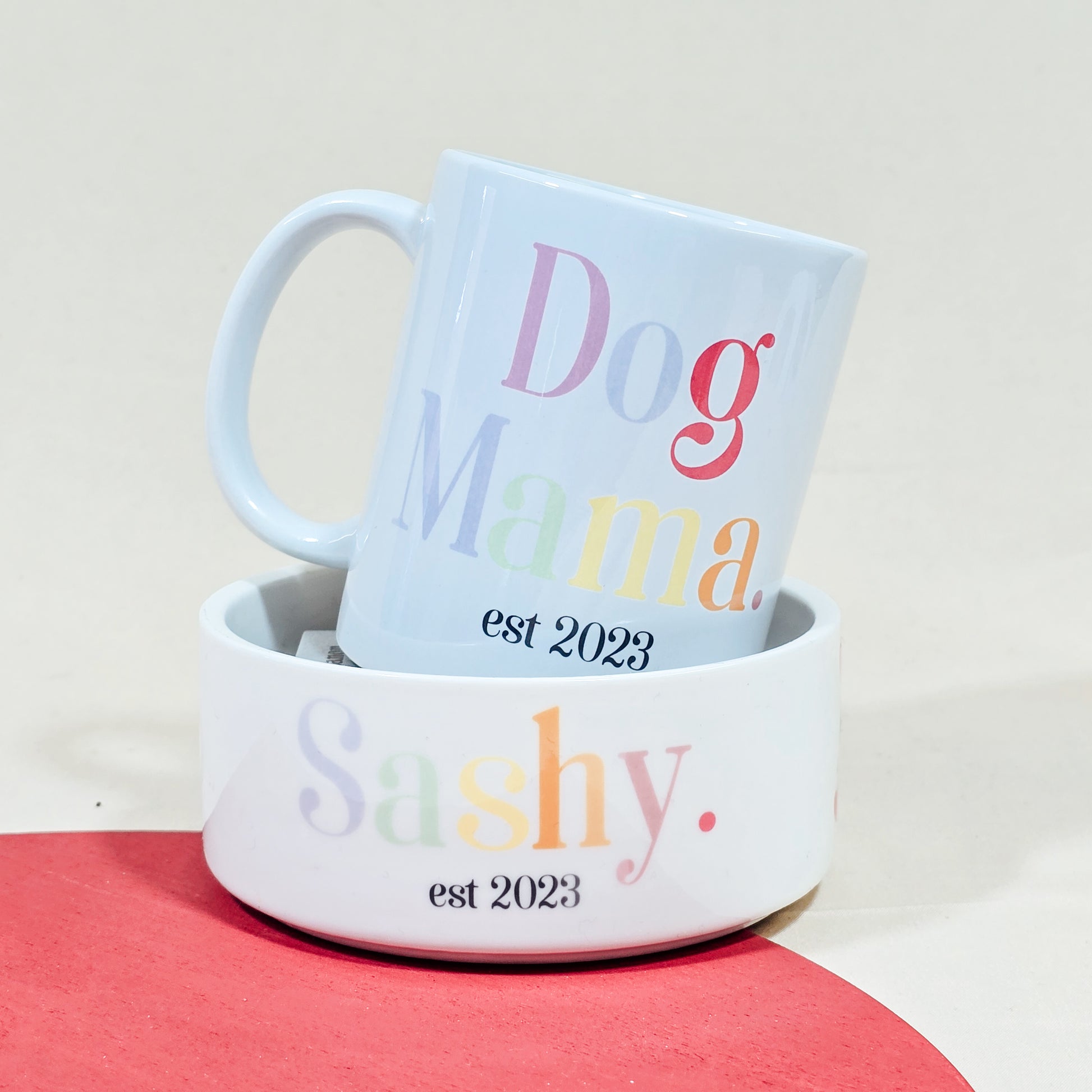 A white ceramic mug with "Dog Mama Est [Date]" in elegant script, available with a matching pet bowl in various sizes.

