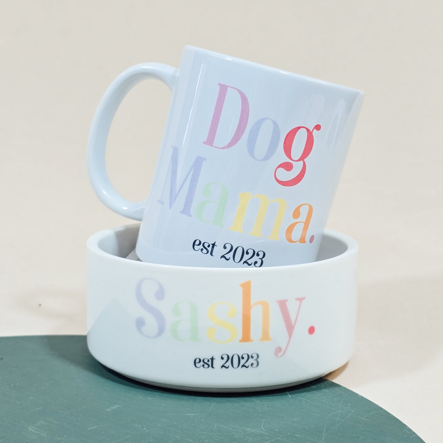 A white ceramic mug with "Dog Mama Est [Date]" in elegant script, available with a matching pet bowl in various sizes.

