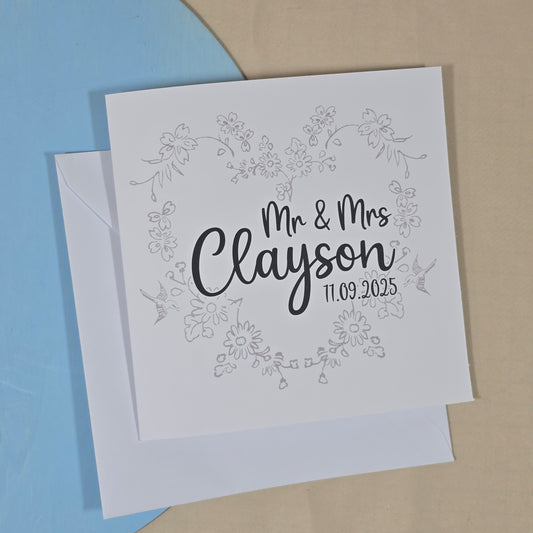 Greeting card with 'Mr & Mrs Clayson' and date on floral design, placed on a blue and beige background.