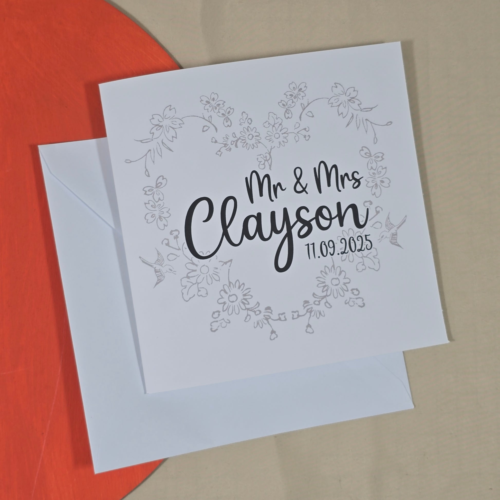 Greeting card with 'Mr & Mrs Clayson' text on a floral wreath design, with a white envelope.