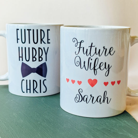 A set of two white mugs, one with "Future Wifey" and a name, the other with "Future Hubby" and a name, perfect for engaged couples.