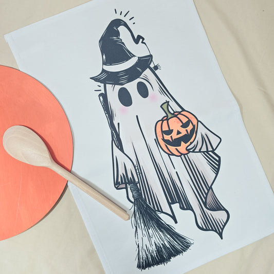 Halloween-themed ghost illustration on a tea towel with a wooden spoon and orange circular object.