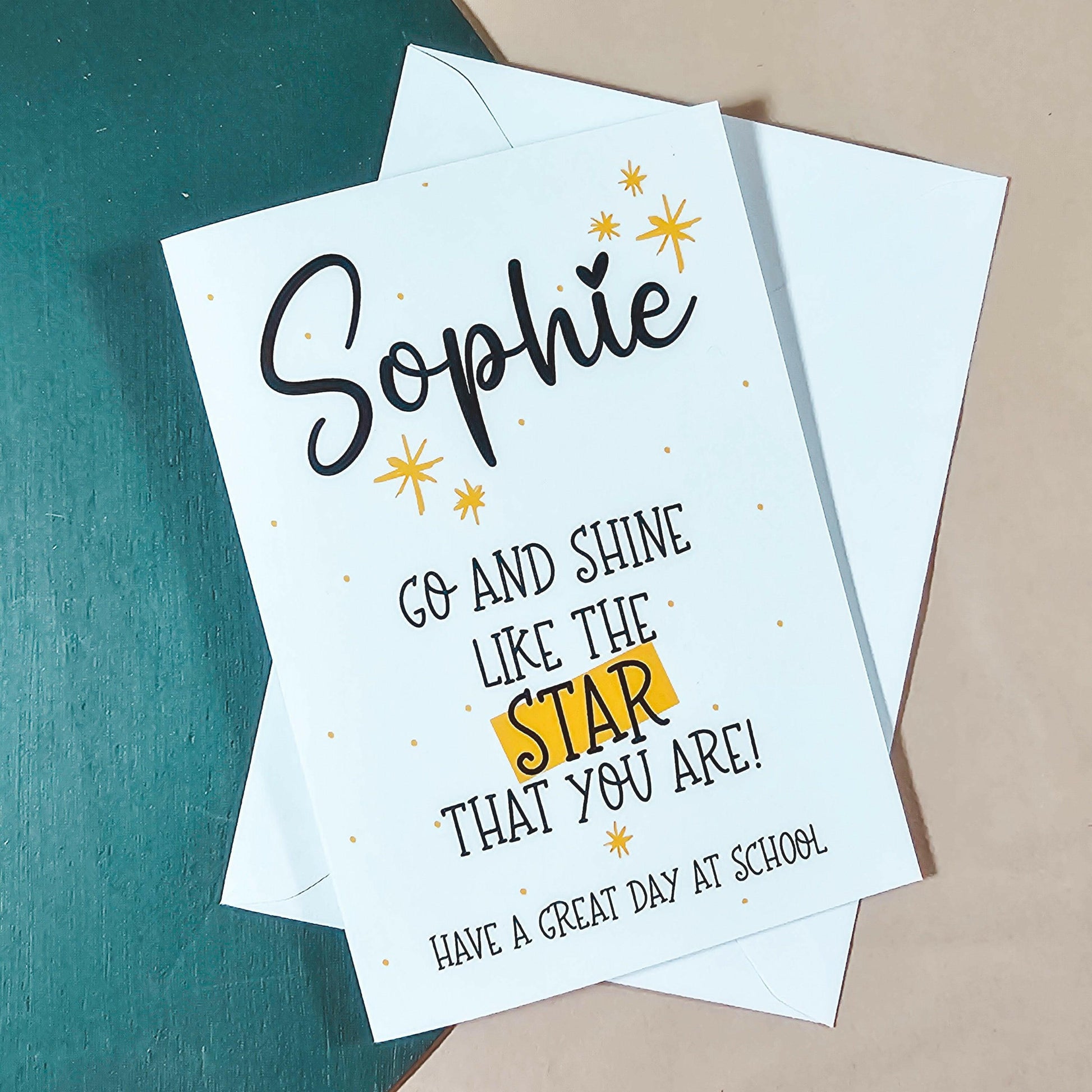 A white card with the text 'go and shine like the star that you are! Have a great day at school' with yellow start motifs on and a personalised name