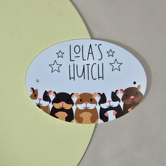 Oval-shaped sign with cartoon hamsters and 'Lola's Hutch' text on a beige background