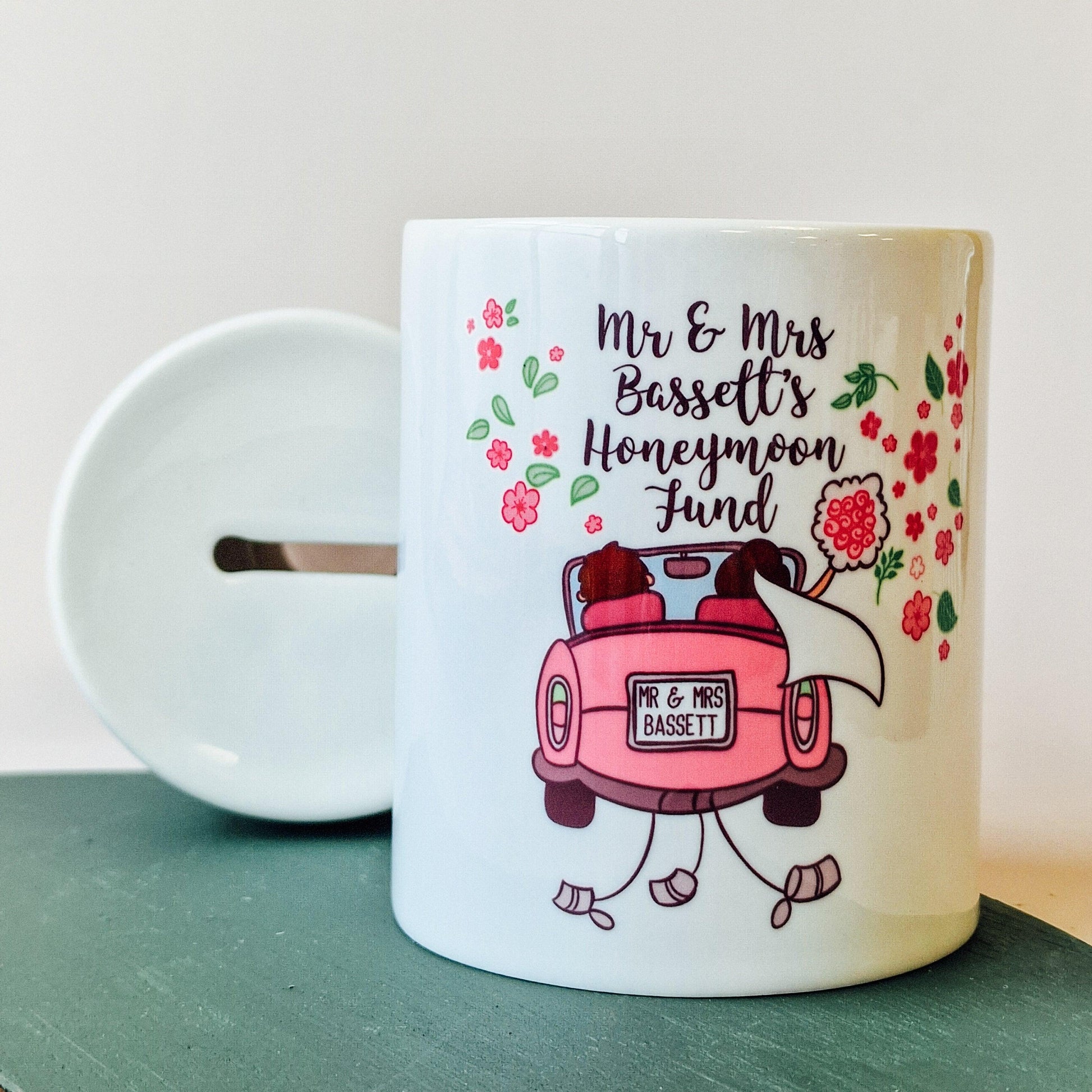 Ceramic money box with "Names Honeymoon Fund" text, featuring a pink car with bride and groom and a customisable number plate, perfect for saving for a honeymoon.