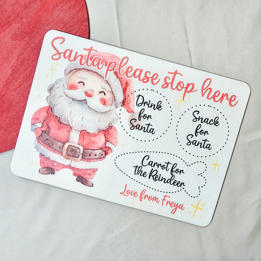 A personalised wooden Santa treat board with engraved spaces for a drink, snack, and reindeer carrot. Available in light or dark wood, with a festive Santa design and personalised name(s) at the bottom.
