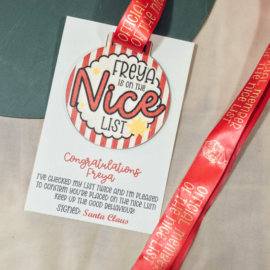 Personalised Christmas Nice List medal with ribbon reading “Official Member of the Nice List,” mounted on A6 card with congratulatory Santa Claus message.