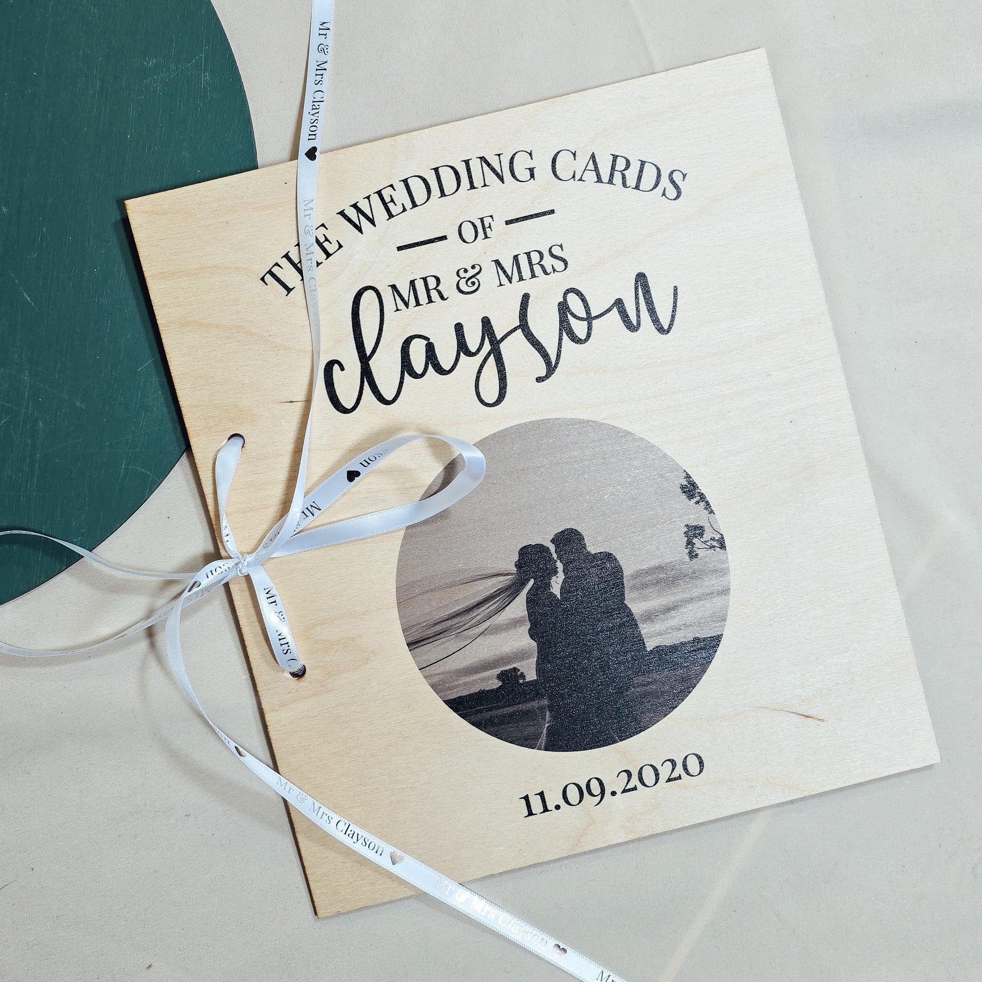 A personalised wedding card book with "The Wedding Cards of Mr & Mrs [Name]" and a wedding photo printed on the wooden cover, tied with a ribbon, perfect for storing special cards.
