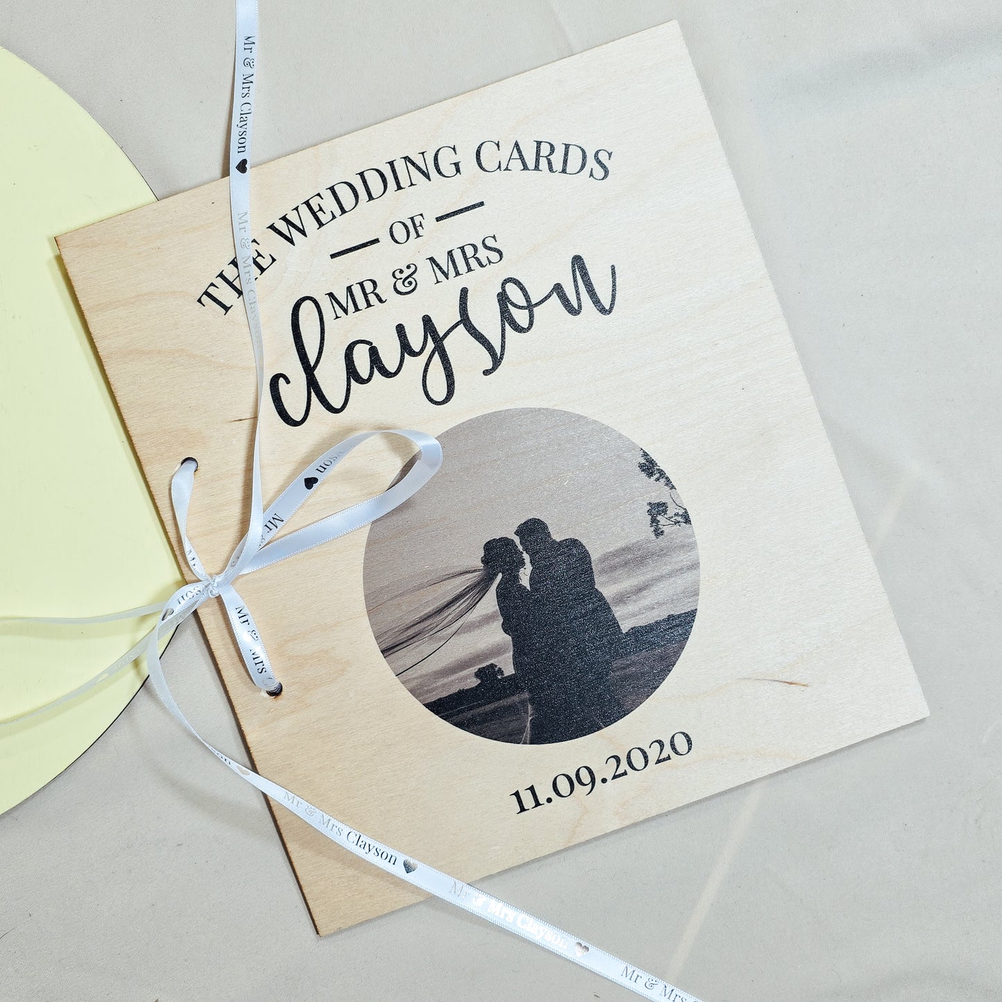 A personalised wedding card book with "The Wedding Cards of Mr & Mrs [Name]" and a wedding photo printed on the wooden cover, tied with a ribbon, perfect for storing special cards.
