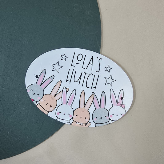 Oval-shaped sign with cartoon bunnies and 'Lola's Hutch' text on a green and beige background